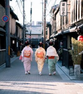 Three women wearing traditional kimonos walk down a historic street in Kyoto, Japan, capturing cultural essence.