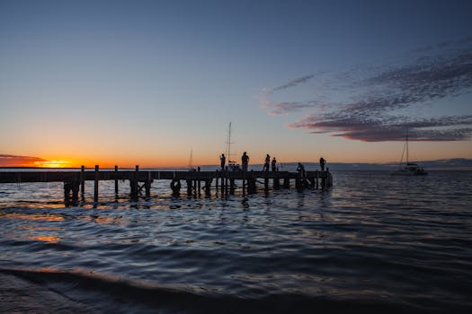 Serene sunset view at Monkey Mia Pier in Australia, featuring silhouettes and tranquil waters.
