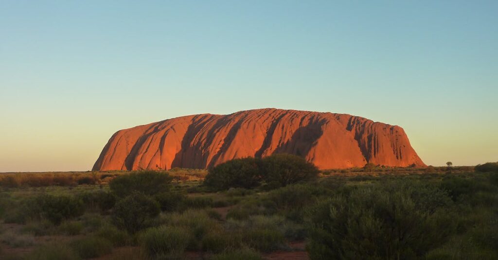 Capture the majestic Uluru rock formation glowing under the sunset. A natural wonder in Australia's Outback.