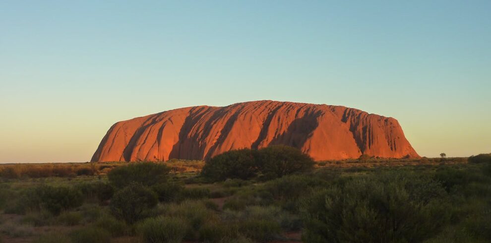 Capture the majestic Uluru rock formation glowing under the sunset. A natural wonder in Australia's Outback.